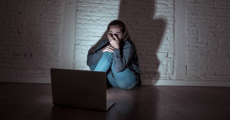 Scared woman looking at her laptop in a darkened room